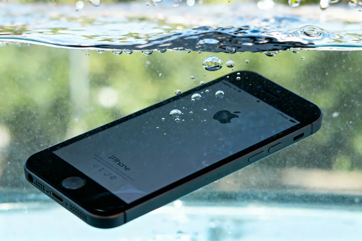 Smartphone noir immergé dans l'eau, bulles autour, écran visible avec logo Apple illuminate.