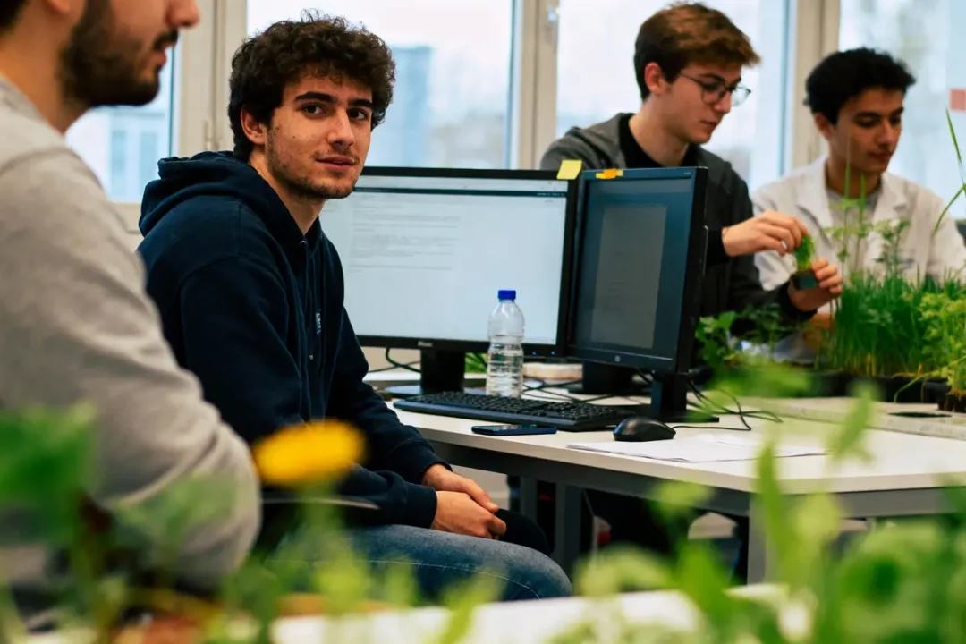 Des étudiants travaillent sur des ordinateurs et manipulent des plantes dans une salle de classe moderne.