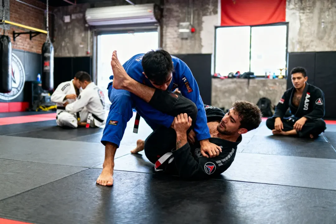 Deux hommes pratiquant le Jiu-Jitsu sur un tatami, observés par d'autres en arrière-plan.