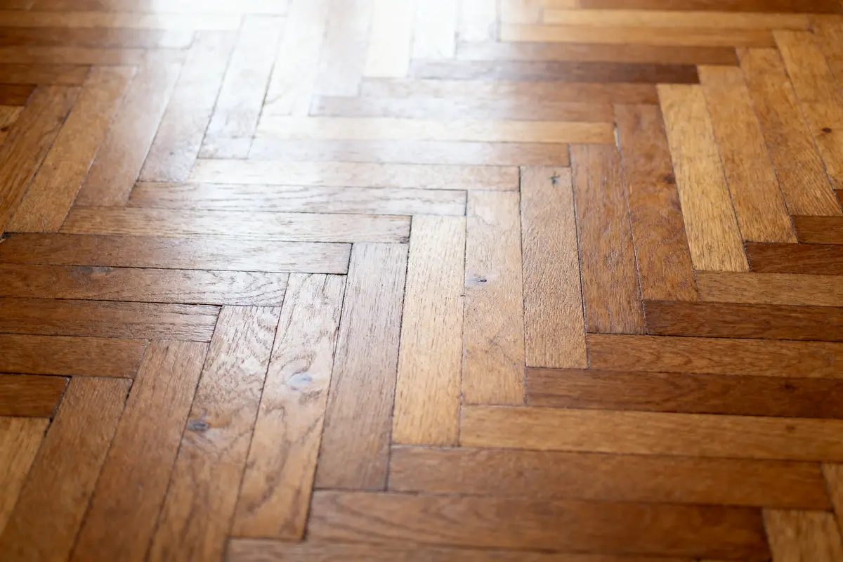 Parquet en bois clair, motif en chevron. Lumière naturelle éclairant la surface brillante.