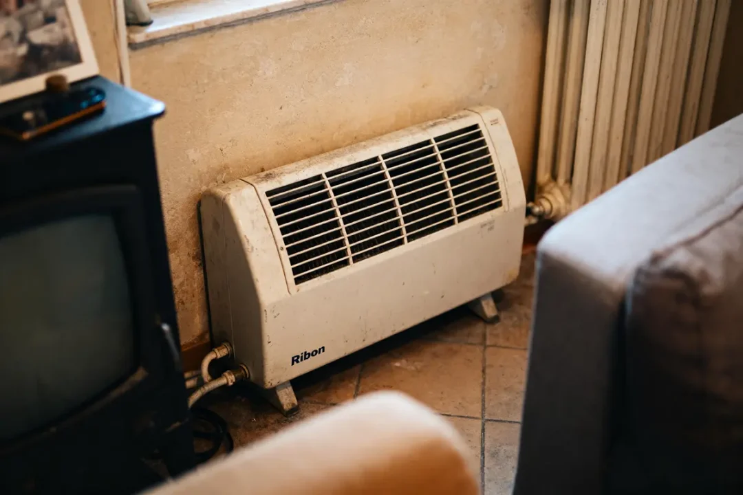 Radiateur électrique blanc sur le sol, près d'un mur beige, entouré de meubles et d'une télévision.