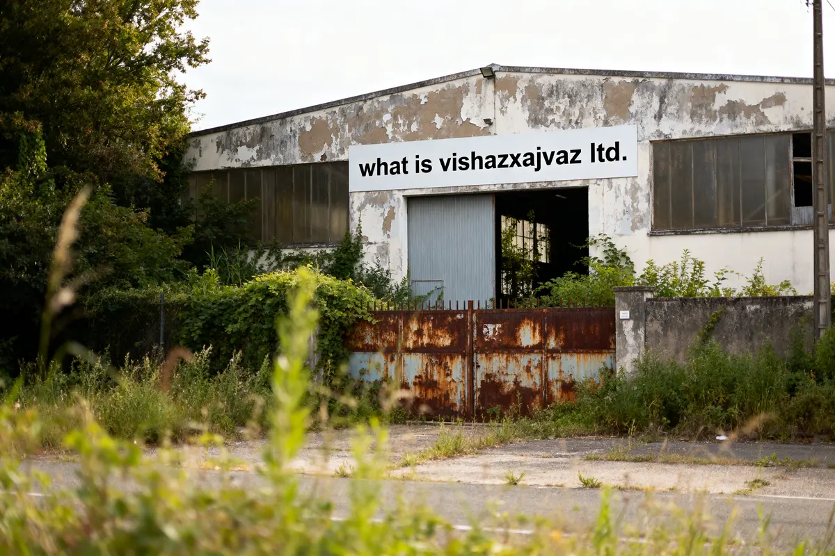 Bâtiment abandonné avec pancarte "what is vishazxajvaz ltd." entouré de végétation, portail rouillé devant.