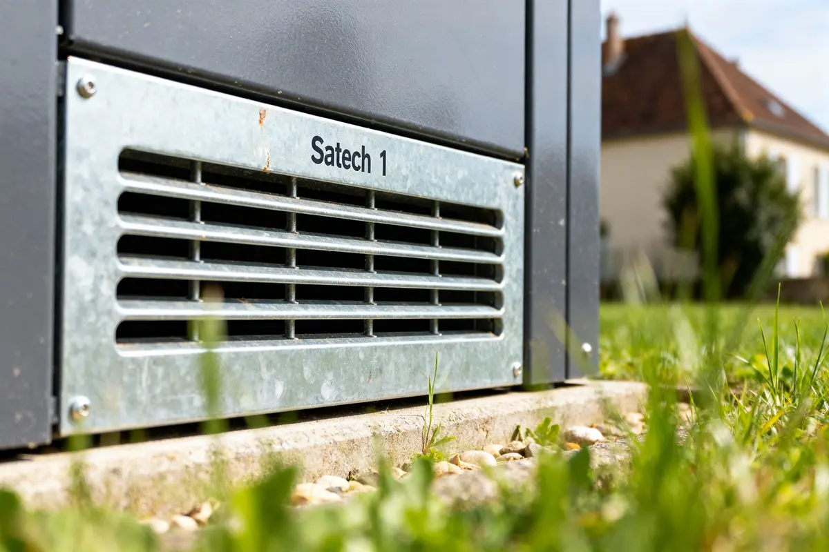 Grille métallique extérieure sur équipement marqué Satech 1 entouré de végétation