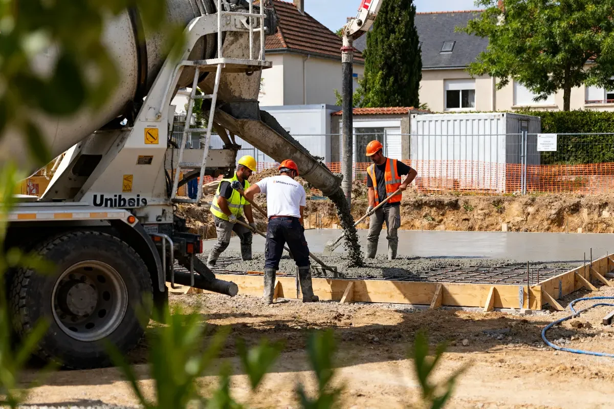 Travailleurs sur chantier coulant du béton avec un camion Unibeton en arrière-plan