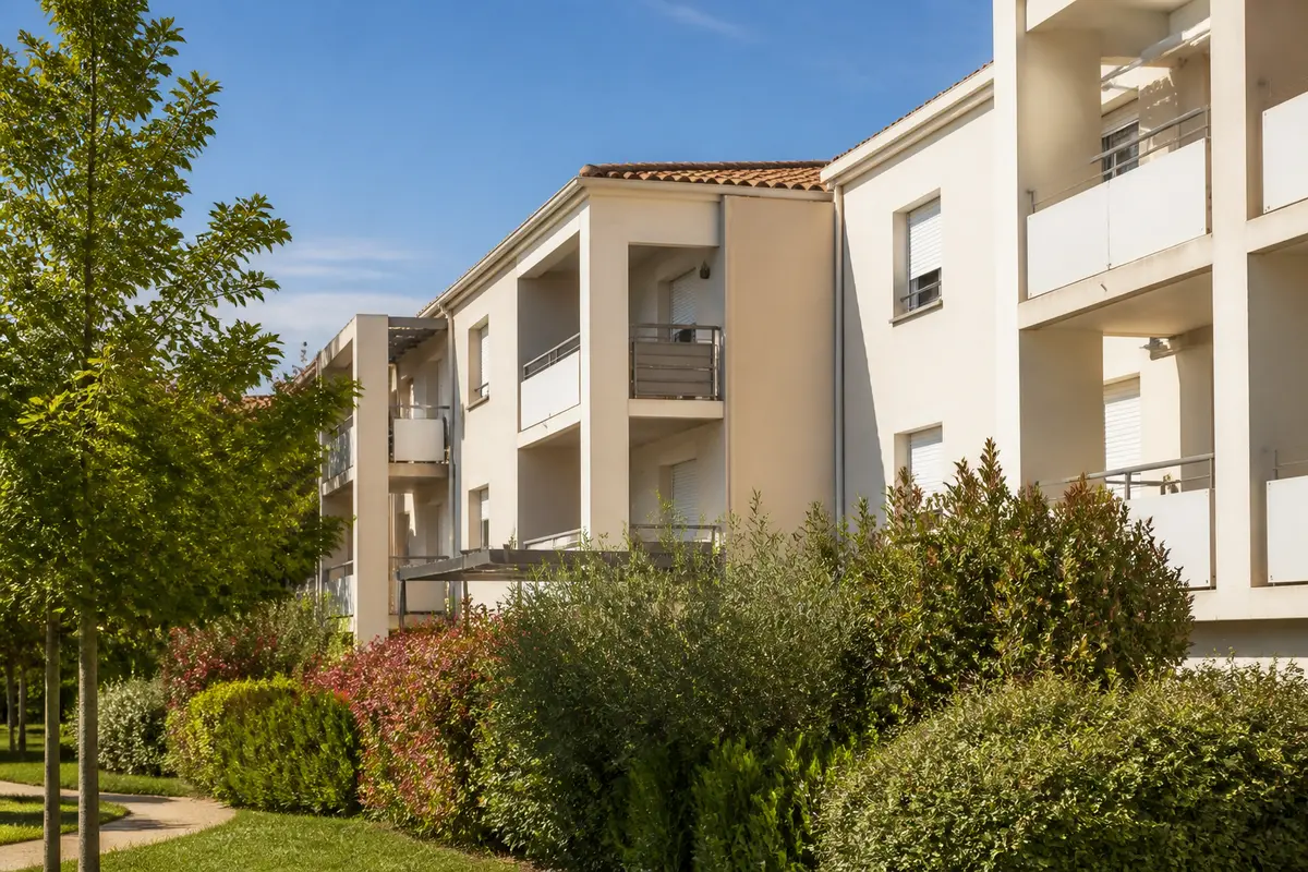 Immeuble résidentiel moderne, arbres et buissons denses, ciel bleu.