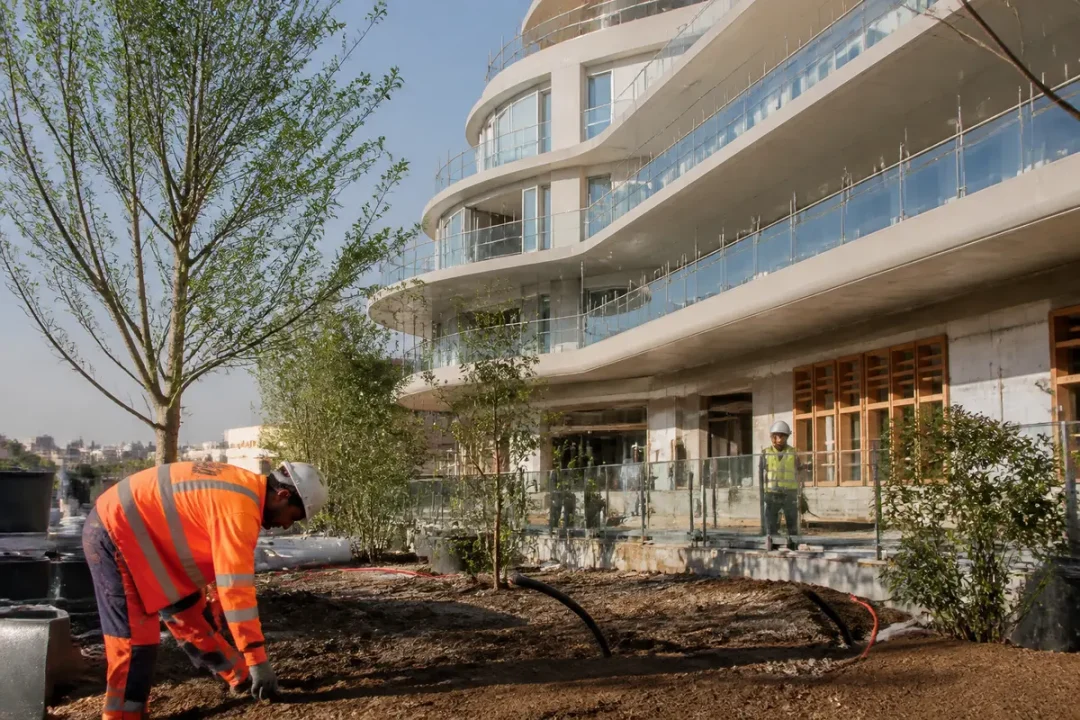Ouvrier en gilet orange travaillant devant un immeuble moderne. Arbre et végétation en aménagement paysager.