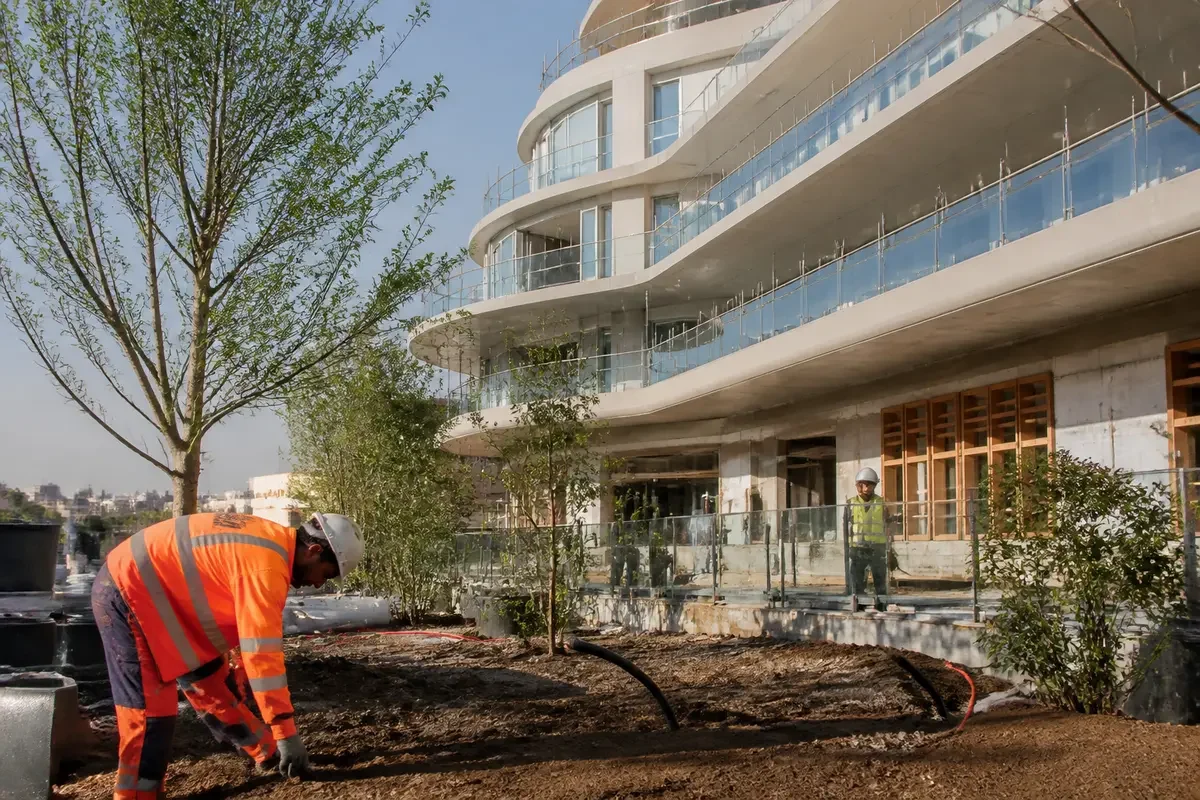 Ouvrier en gilet orange travaillant devant un immeuble moderne. Arbre et végétation en aménagement paysager.