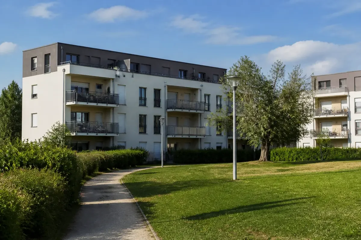Immeubles résidentiels modernes avec balcons, entourés de verdure et chemin piéton, sous un ciel bleu.