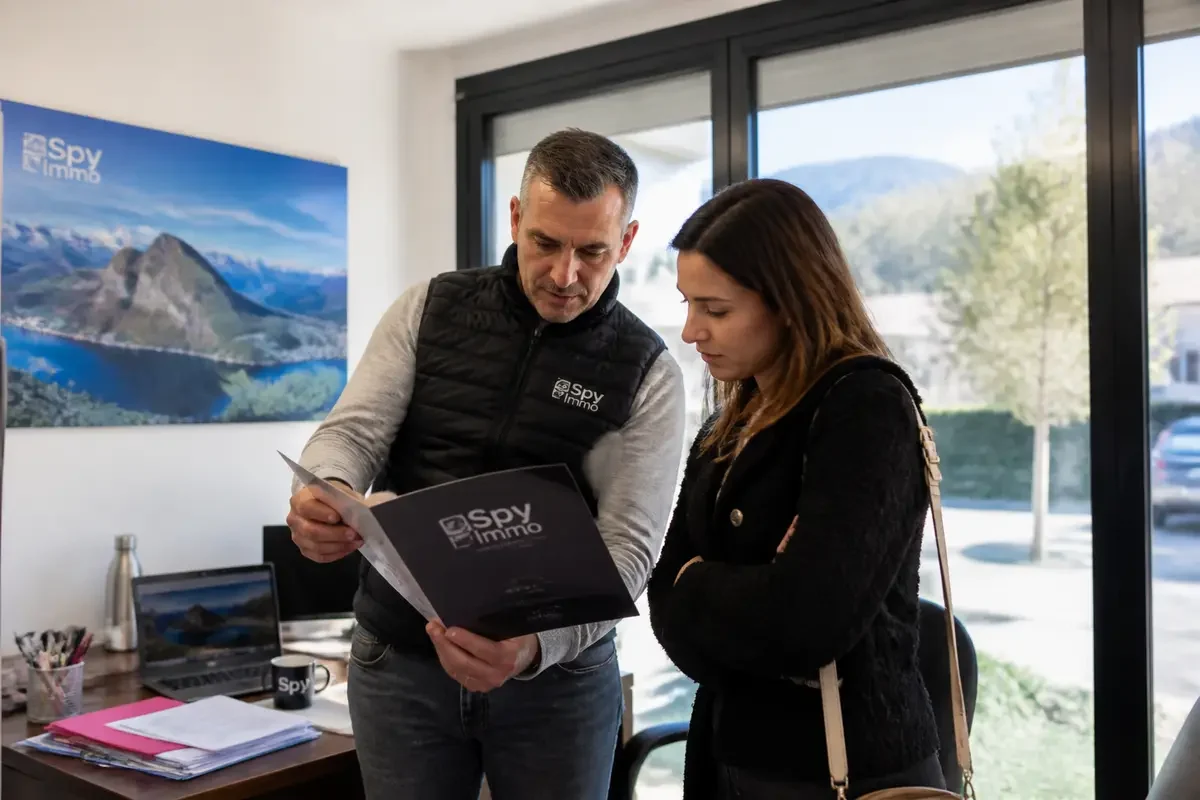Un homme et une femme discutent de documents dans un bureau immobilier lumineux.
