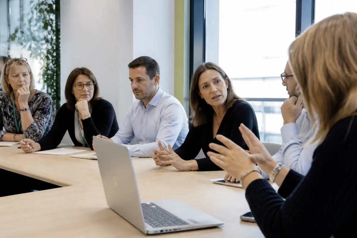 Un groupe de personnes lors d'une réunion professionnelle autour d'une table, avec un ordinateur portable.